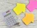 Kalkulator, żarówka i kolorowe strzałki sugerują analizę przyszłej ceny prądu 2026 za 1 kWh.