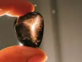 Dedos sostienen una piedra oscura con destellos dorados. ¿Qué pasa si se rompe una piedra energética? Quizás solo se dispersa su luz.