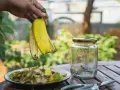 Ręka trzyma skórki bananów nad talerzem z ich kawałkami. Obok stoi słoik, gotowy na nawóz z bananów do jakich roślin.