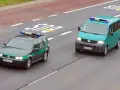 Dwa pojazdy uprzywilejowane Straży Granicznej, zielony kombi i turkusowy van, jadą drogą.