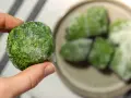 Gefrorene Spinat-Portionen, bereit zum **Spinat zubereiten**. Eine Hand hält einen gefrorenen Spinat-Kloß, im Hintergrund weitere auf einem Teller.