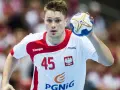 Michał Szyba, numer 45, w białej koszulce z czerwonymi elementami, trzyma piłkę do piłki ręcznej.