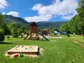 Plac zabaw dla dzieci na terenie radków camping. Piaskownica, zjeżdżalnie i drabinki w otoczeniu zieleni i gór.
