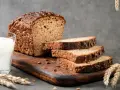 Chleb proteinowy z ziarnami, pokrojony na kromki, obok szklanka mleka i kłosy zboża. Idealny na zdrowe śniadanie.