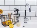 Kosz z cytrynami, szczotką i butelką octu obok kranu w łazience.