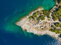 Widok z lotu ptaka na kemping Riviera Makarska. Kamieniste wybrzeże, turkusowa woda i zielone drzewa otaczają liczne przyczepy kempingowe i samochody.