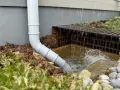 Un tuyau blanc dirige l'eau de pluie vers un drain. Le système d'évacuation eau pluviale fonctionne bien, empêchant l'eau de stagner près de la maison.