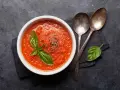 Eine Schüssel mit leckerer, italienischer Tomatensauce, garniert mit Basilikum und Pfeffer. Daneben liegen zwei Löffel.