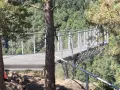 La passerelle himalayenne de Grazac offre une vue imprenable sur la vallée verdoyante. Une personne marche sur la structure métallique.