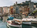 Boats bob in the harbor of a colorful Italian Riviera town, with ancient castles overlooking the vibrant buildings.