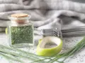 A jar filled with dried chives, showcasing how to dry chives for long-term storage. Fresh chives and kitchen tools are nearby.