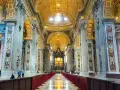 Interior of a grand basilica in Rome, with ornate golden ceilings, marble columns, and a long aisle lined with red velvet.