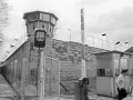 Wachturm und Grenzbefestigung der deutschen demokratischen Republik. Ein Wachmann steht neben einer Schranke und einem Kontrollhäuschen.