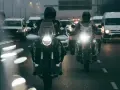 Dwóch motocyklistów w kaskach jedzie w deszczu. Ich motocykle mają włączone światła, a droga polna jest mokra i błyszcząca.