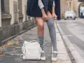 Stylizacja z długimi skarpetkami damskimi, biały plecak i jesienne liście na chodniku.
