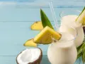 Dwa orzeźwiające koktajle pina colada z kawałkami ananasa i kokosem na niebieskim tle.