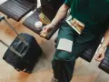 Osoba w zielonej koszulce siedzi na lotnisku z walizką i kawą, jedząc kanapkę. Czy można zabrać do samolotu kanapki? Tak, jak widać!