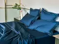 Letto matrimoniale con copriletto blu scuro e cuscini coordinati, rifiniti con bordi bianchi. Ideale per conoscere le misure copriletto matrimoniale.