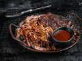 Saftiges pulled pork mit BBQ-Sauce und Beilagen auf einem Teller. Ein Gabel liegt daneben.
