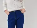 Gros plan sur une personne portant un pull blanc et un pantalon en jean bleu avec les mains dans les poches.