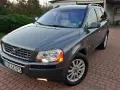 Szary Volvo XC90 z silnikiem V8, zaparkowany na podjeździe z kostki brukowej, otoczony zielenią.