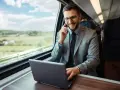 Biznesmen w garniturze rozmawia przez telefon i pracuje na laptopie w pociągu.