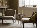 Przytulny salon w stylu angielskim. Dwa fotele, stolik z zapaloną świecą, kosz z pledem i stylowy mebel pod oknem.