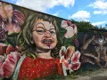 En väggmålning med en busig flicka omgiven av blommor ger graffiti inspiration. Bredvid syns ett mystiskt ansikte med händer.