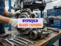 Mechanik trzyma skrzynię biegów, na stole leżą klucze. Widoczny wysprzęglik centralny, objawy i naprawa.
