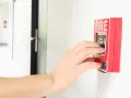 Mano activando la alarma de incendios. Instrucciones claras: "PULL DOWN" para saber cómo apagar alarma de incendios.