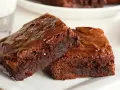 Dos deliciosos trozos de brownie de chocolate, con una textura húmeda y crujiente por encima, listos para ser disfrutados.
