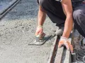 Pracownik wygładza świeży beton, dbając o odpowiednie suchy beton proporcje. Ręce w rękawiczkach trzymają kielnię.