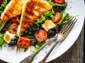 Pyszna sałatka z grillowanym halloumi, pomidorkami koktajlowymi i czarnymi oliwkami na rukoli. Idealna na lekki posiłek.