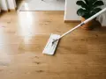 Ein Wischmopp reinigt einen glänzenden Holzboden. Das Laminat erstrahlt nach der Reinigung.
