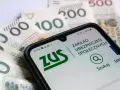 Zasiłek macierzyński 80 czy 100% i 60%? Telefon z aplikacją ZUS na tle polskich banknotów.