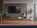 Un salon moderne avec une TV fixée au mur sans voir les fils. Un meuble bas en bois, des livres et une plante verte complètent la décoration.