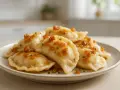 Pyszne pierogi ruskie z ziemniakami i serem, polane skwarkami i szczypiorkiem, na talerzu.