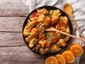 Sabroso pollo a la naranja, cubierto con salsa brillante y cebollín picado, servido con rodajas de naranja fresca.