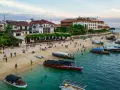 Tanzański szyling na plaży w Stone Town, Zanzibarze. Ludzie odpoczywają, bawią się i pływają, a łodzie czekają na turystów.
