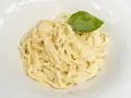 Un plato de spaghetti a la carbonara con nata, cremoso y adornado con una hoja de albahaca fresca.