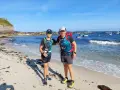 Dos excursionistas, padre e hijo, disfrutan de la playa en la etapa Baiona Vigo. El mar azul y el cielo despejado acompañan su aventura.