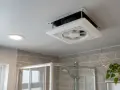Extractor de baño siempre encendido, ventilando el espacio sobre la ducha. Una luz empotrada ilumina el techo.