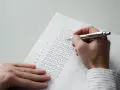 Dłoń z długopisem wypełnia ankietę z polami wyboru.