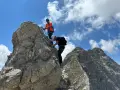 Zwei Bergsteiger meistern den **Hindelanger Klettersteig** auf felsigem Grat unter blauem Himmel mit Wolken.