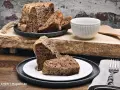 Zwei Stücke eines rustikalen, dunklen Diabetiker Kuchens auf einem Teller, daneben ein ganzer Kuchen mit angeschnittenen Scheiben.