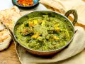 Ein köstliches Palak Paneer in einer Kupferschale, serviert mit Fladenbrot und Chiliflocken.
