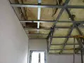 Konstrukcja podwieszanego sufitu z metalowymi profilami i pianką izolacyjną. Widać fragmenty ścian i okna.