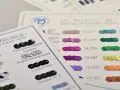 Échantillons de sequins pour faire un motif. Des sequins noirs, argentés, roses, violets, verts, jaunes et orangés sont présentés sur des fiches de couleurs.