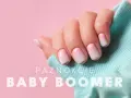 Dłoń z paznokciami hybryda baby boomer w delikatnym różowo-białym ombre, na tle pudrowego różu i turkusowego materiału.