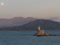 Faro solitario su un'isola sarda, con montagne sullo sfondo e luna piena. Perfetto per itinerari moto Sardegna 7 giorni.